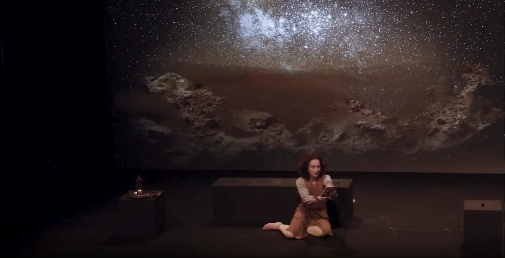 Élodie Tisserand assise sur scène, face à une immense projection de ciel étoilé, dans « Les Rois Mages ».